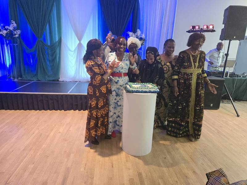 Women in African print dresses gathered around the anniversary cake at the SALONE@65 celebration
